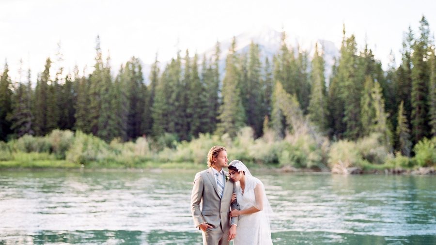 Canmore elopement - beautiful bride and groom standing in front of Bow River and mountains in the background. 